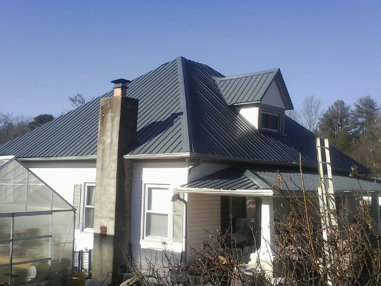 Dark blue standing seam metal roof on a white farmhouse with dormer — Slate & Tile Roof Repair by Roofing Brothers in Hornell