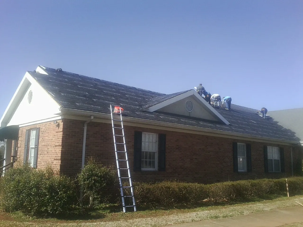 Crew tearing shingles off a brick ranch roof with a ladder set — Emergency Roof Repair work by our crew in Hornell