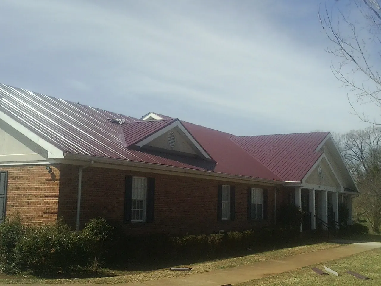 Red metal roof with gabled entries on a long brick building, from a Hail Damage Roof Repair job in Hornell