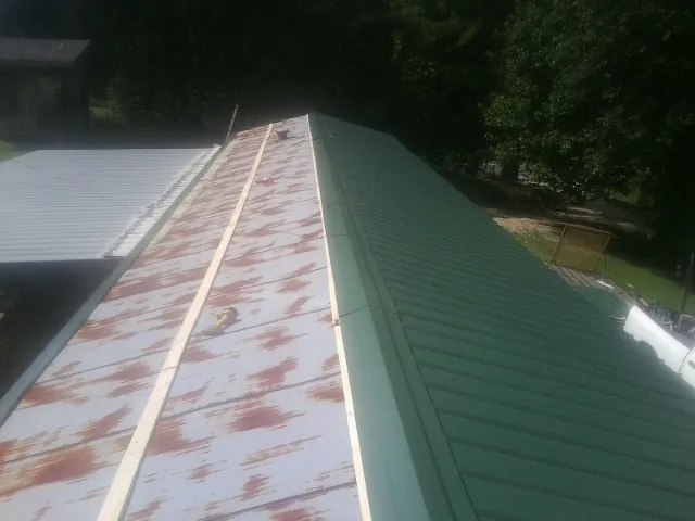 Old rusted panels beside newly installed green metal roofing — Wind Damage Roof Repair by Roofing Brothers in Hornell