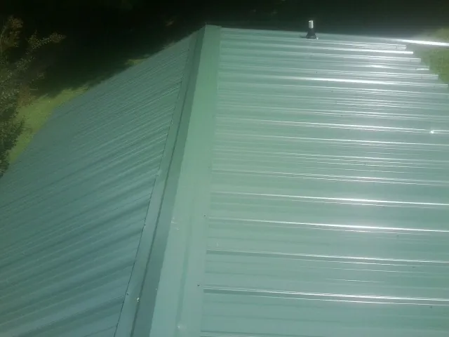 New green metal panels meeting at the ridge of a roof — Flat Roof Repair work by our crew in Hornell