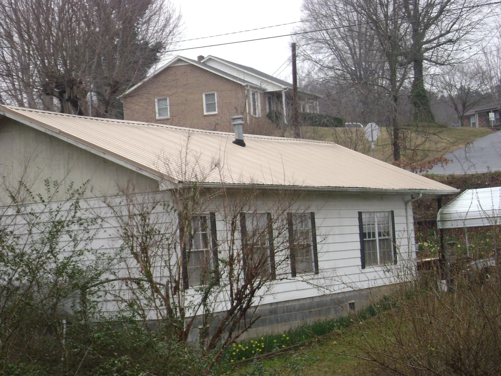 Tan metal roof on a white sided house set into a hillside — Commercial Roofing by Roofing Brothers in Hornell