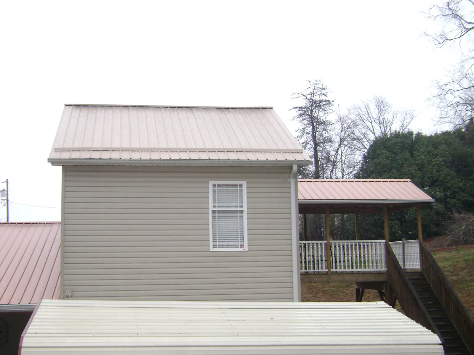 Tan metal roofs on a two story addition and attached porch, from a Roof Replacement job in Hornell