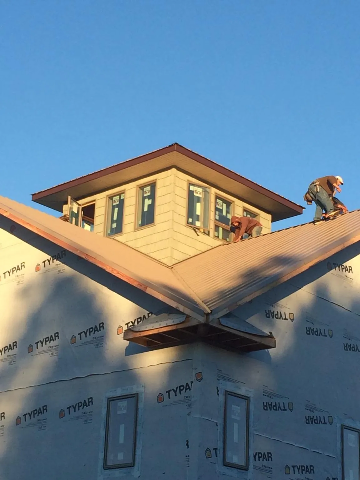 Roofers working around a rooftop cupola on a new metal roof at sunset — Roof Waterproofing in Hornell by Roofing Brothers